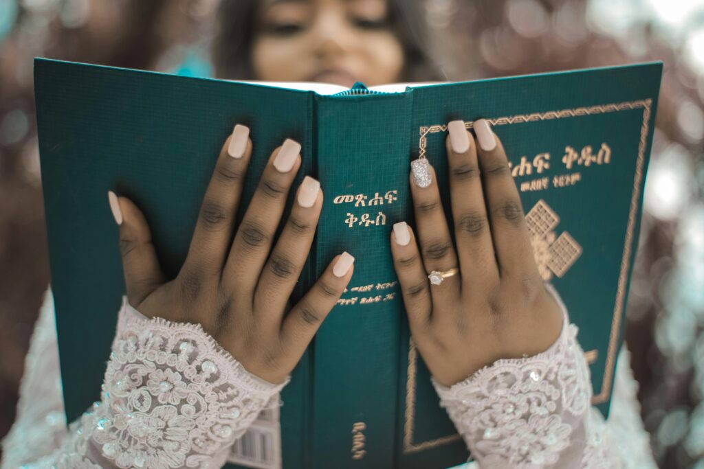 Bride with elegant lace gloves holding and reading a religious book outdoors, symbolizing faith and tradition.