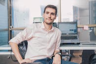 Confident young man in shirt working in modern office with laptop and desk accessories.